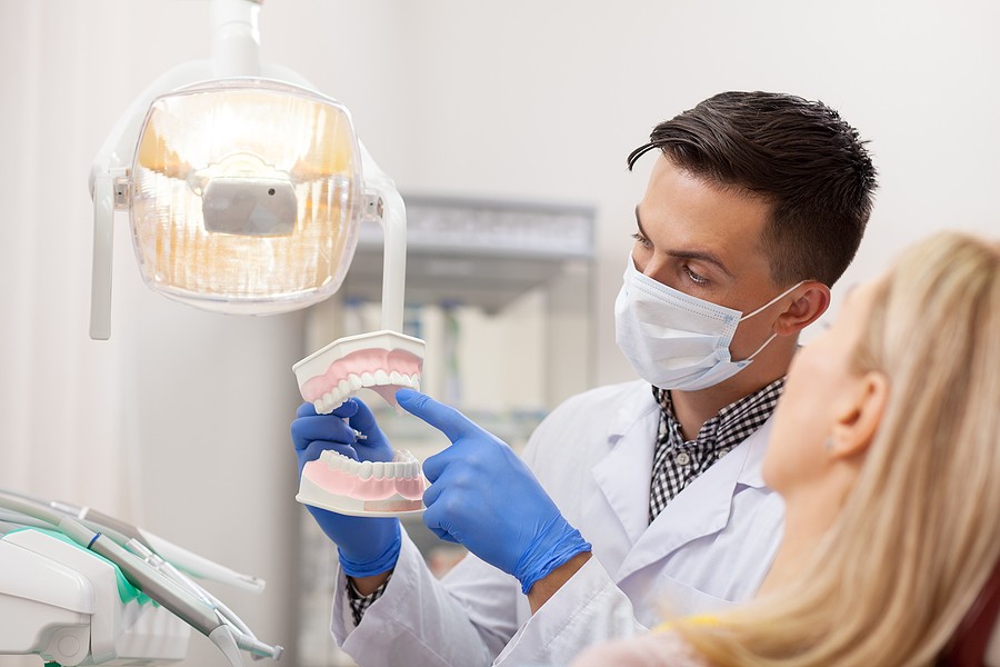 A dentist shows a patient an example of an exposed tooth root.
