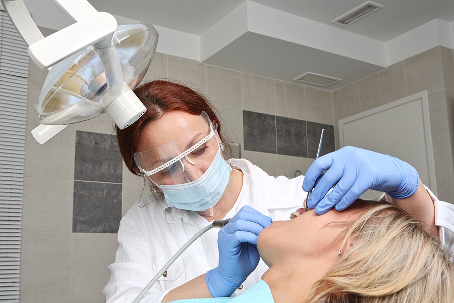 Dentist performing gum surgery on a patient using dental tools, with protective mask and gloves