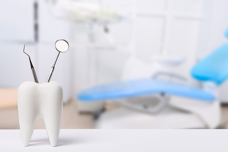 Dental mirror resting in a tooth-shaped holder with a blurred dental chair in the background