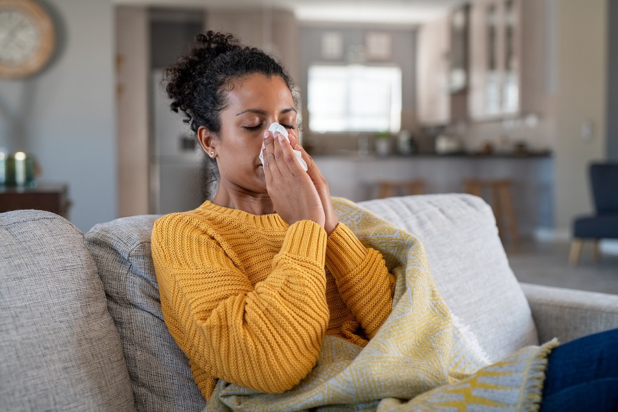 Woman with seasonal allergies blowing her nose on the couch