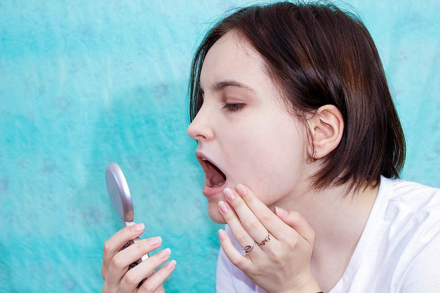 Woman examining her teeth in a mirror for possible hairline cracks
