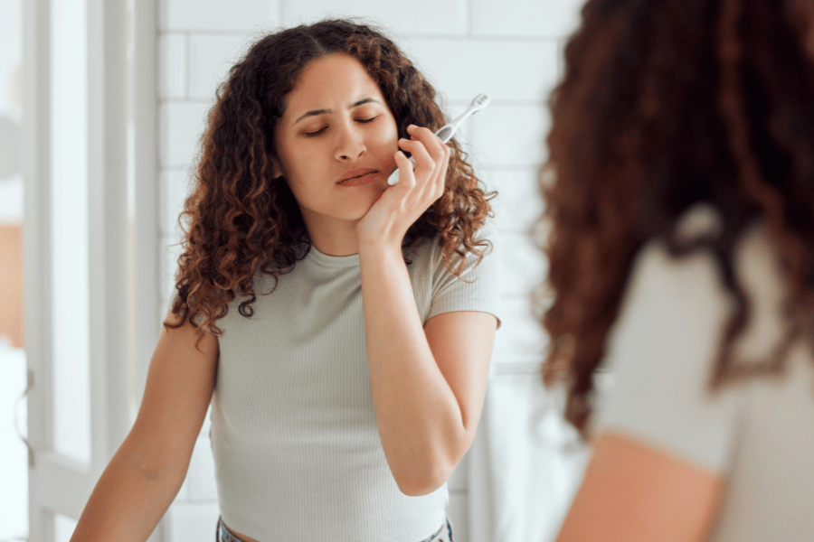 Woman experiencing tooth pain while looking in bathroom mirror